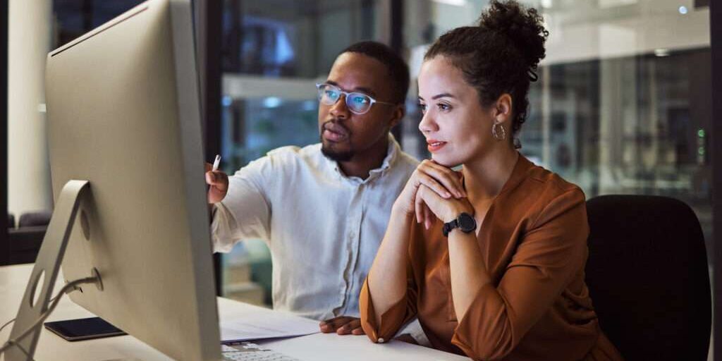 Business training, night planning and employees talking about corporate proposal on internet in dark office at night. African workers working on partnership on the web with computer during overtime.