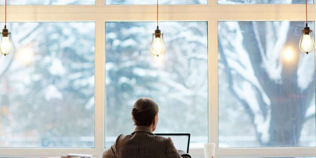 Back view of elegant-looking entrepreneur writing email to her business partner while enjoying delicious coffee and picturesque view of cyber cafe